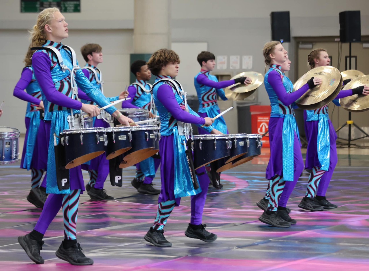 Winter percussion students perform holding drums, sticks, and cymbals